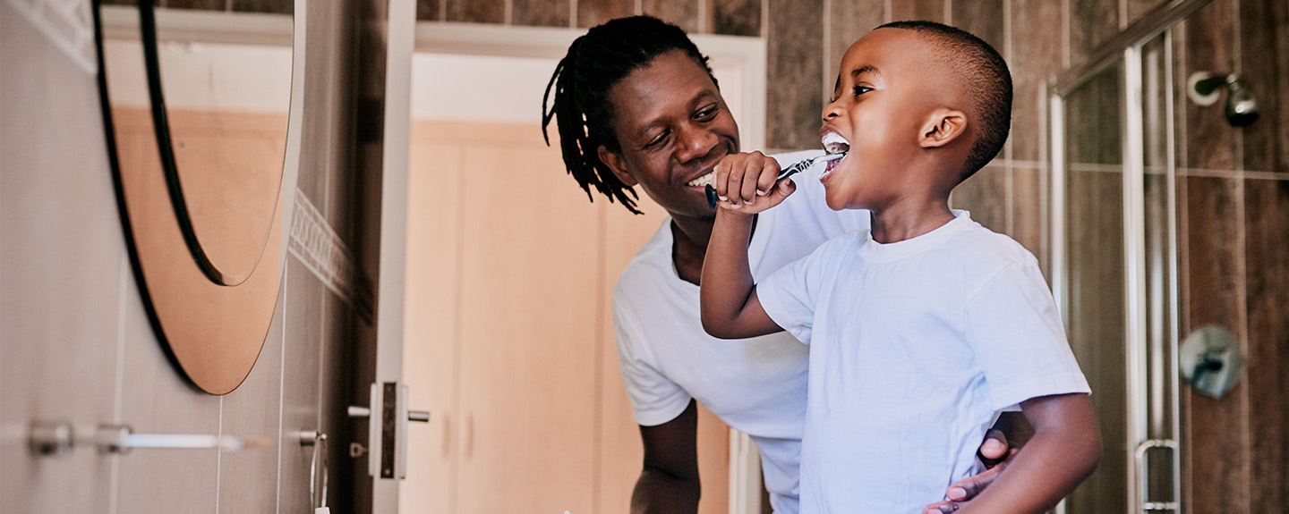 a father looks on as his school-age son brushes his teeth